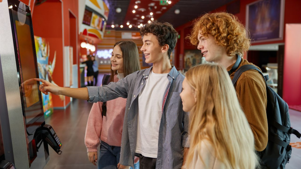 Teens using a self-service kiosk at an entertainment venue.