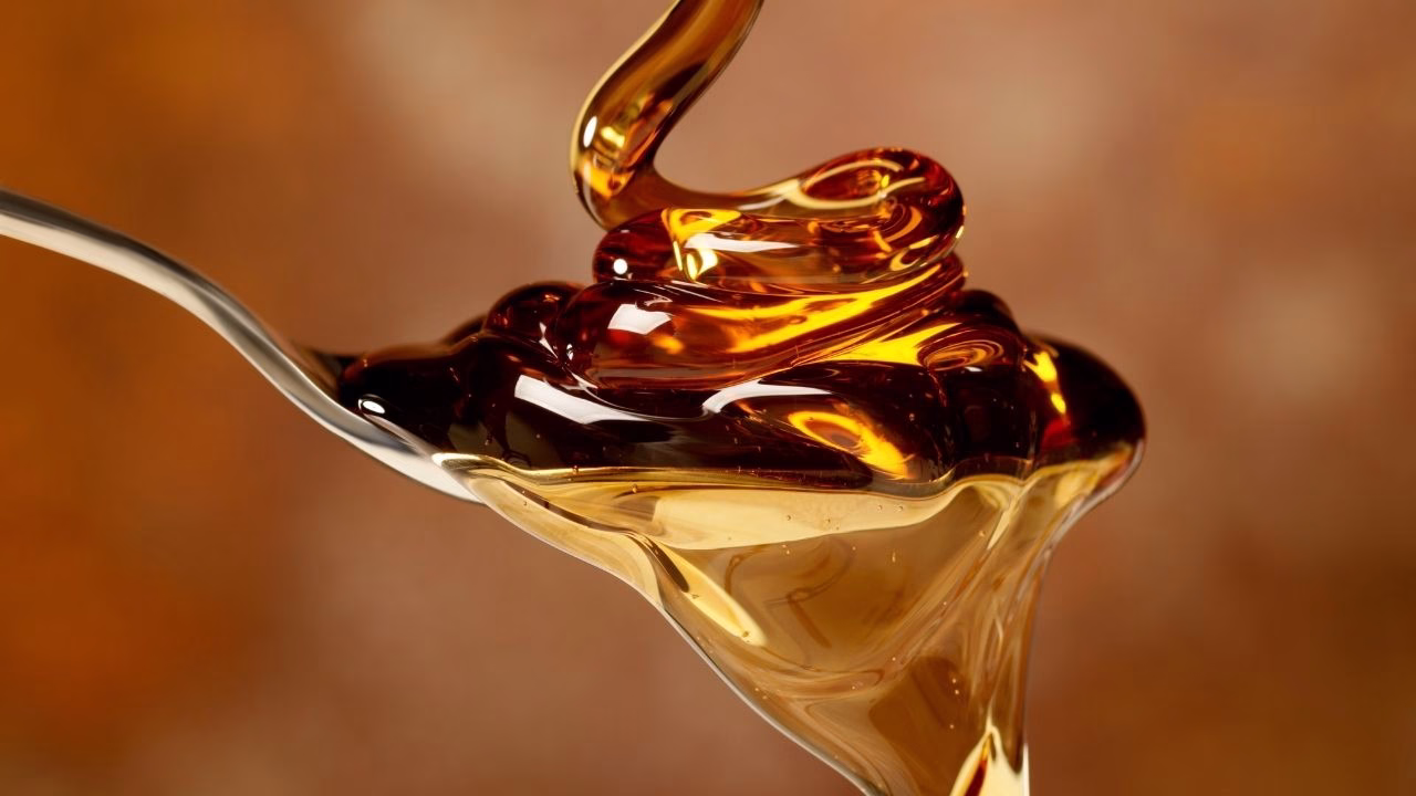Golden syrup drizzling onto a spoon with a warm background.