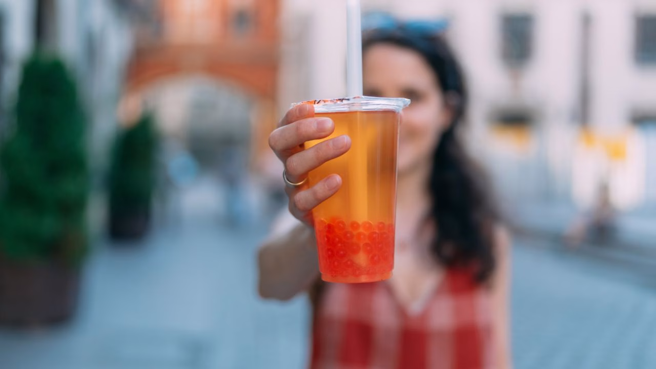 Woman holding a cup of fruit tea with red popping pearls on a city street